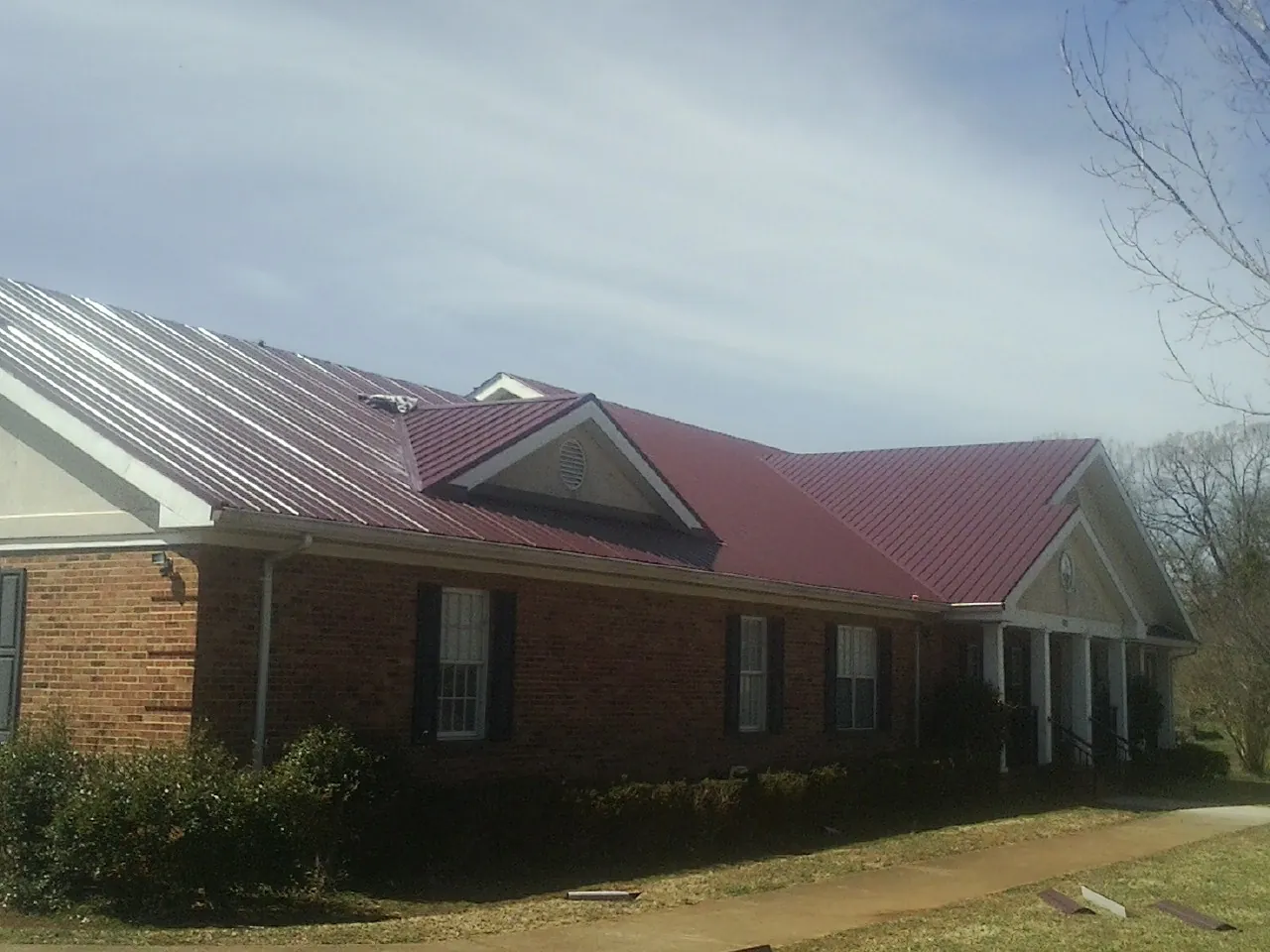Red metal roof with gabled entries on a long brick building, from a Hail Damage Roof Repair job in Santa Clara